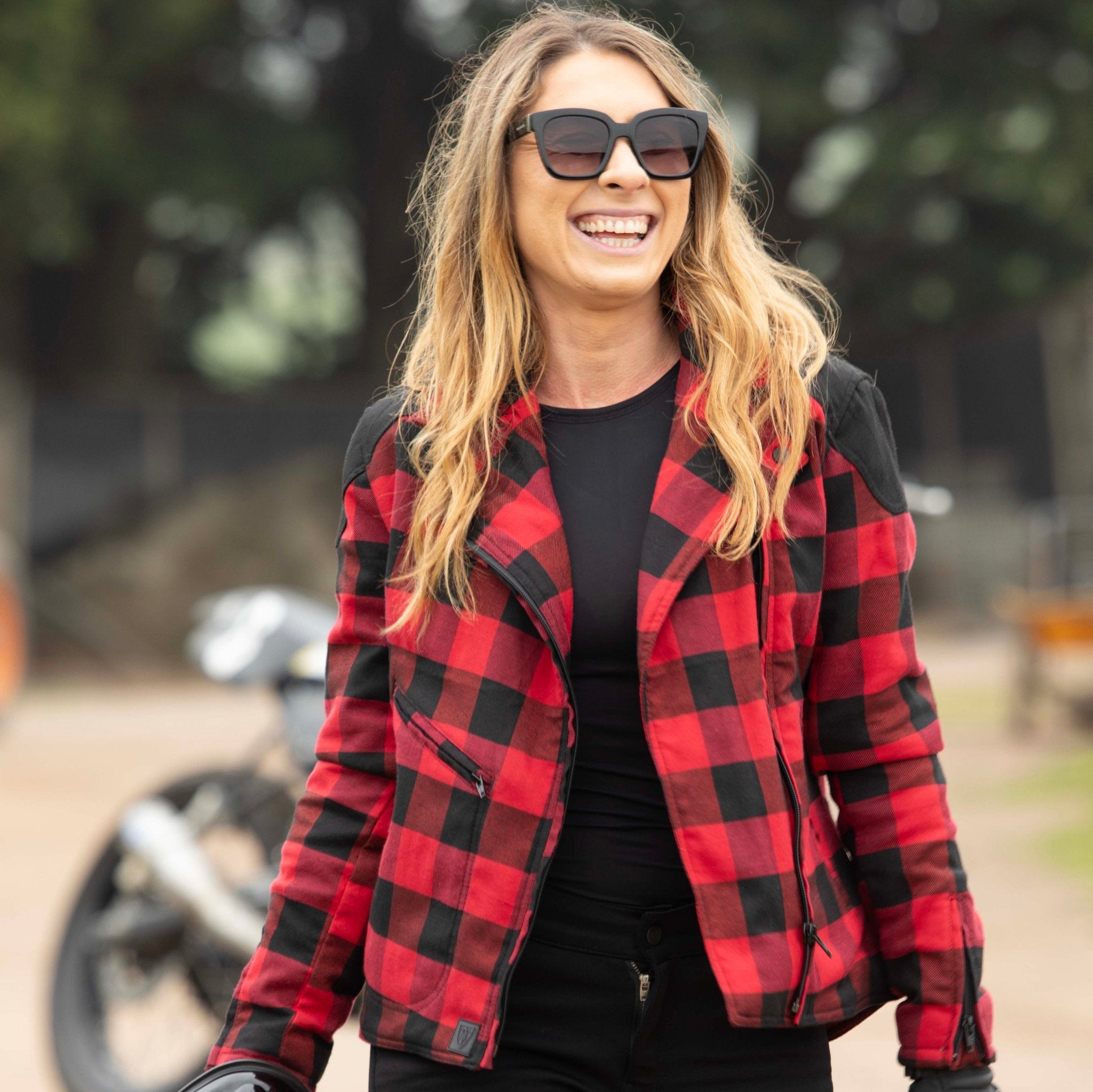 smiling woman with sunglasses wearing  red and black flannel-style women's jacket from moto girl