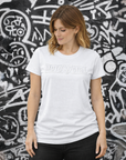 Woman wearing a white t-shirt with 'Moto Girl' text against a graffiti-covered wall.