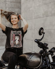 Woman sitting on a Motorcycle wearing  a T-shirt with a women wearing a Motorcyclehelmet print and with the text "Wild dust sisters woman rider" and "Speed Goddess"