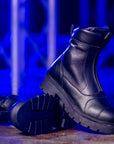 Black leather boots with thick soles on a textured surface with blue lighting.