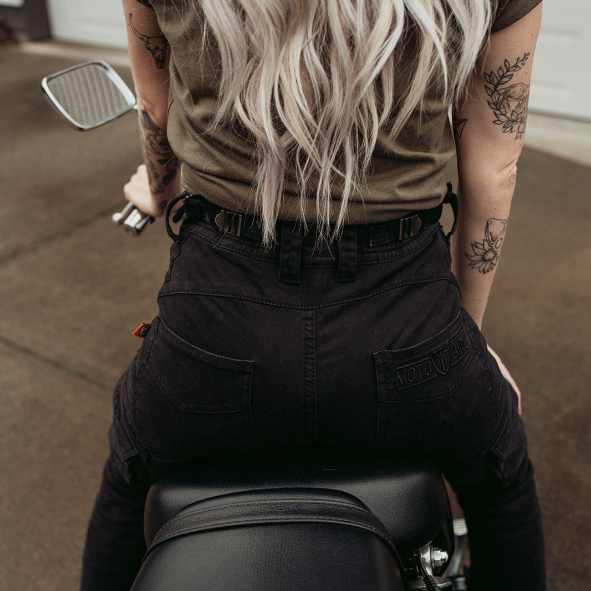 a back of a woman siting on a motorcycle wearing adjustable waist black mc pants
