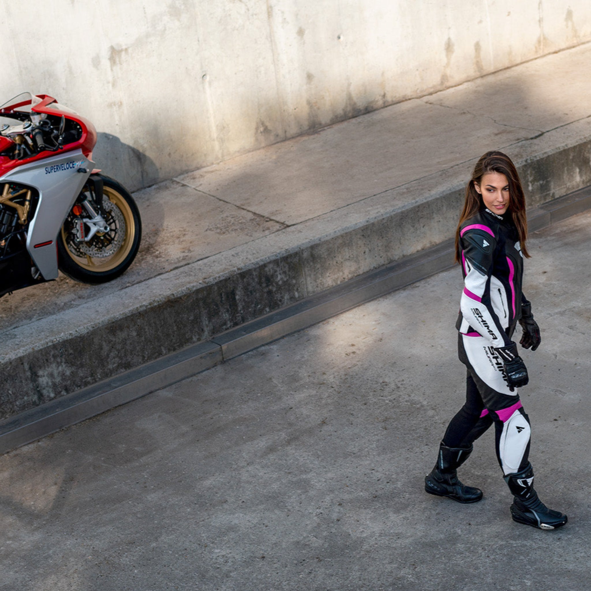 Young woman wearing black, white, pink SHIMA motorcycle  leather suit with her red motorcycle