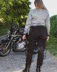 Person standing next to a motorcycle with a helmet, wearing a light gray shirt and black pants.