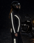 Person wearing a reflective jacket standing next to a motorcycle in the rain.