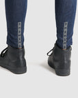 a close up of a woman's legs wearing blue motorcycle jeans and black shoes