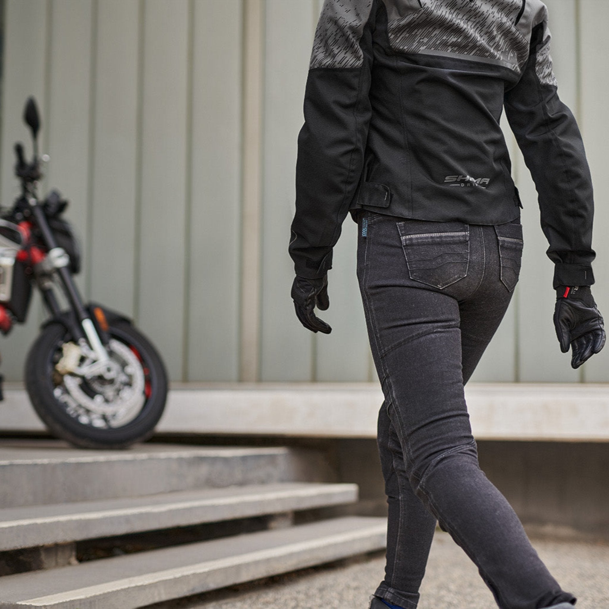 a woman walkig towards her motorcycle wearing grey women's motorcycle jacket from SHIMA
