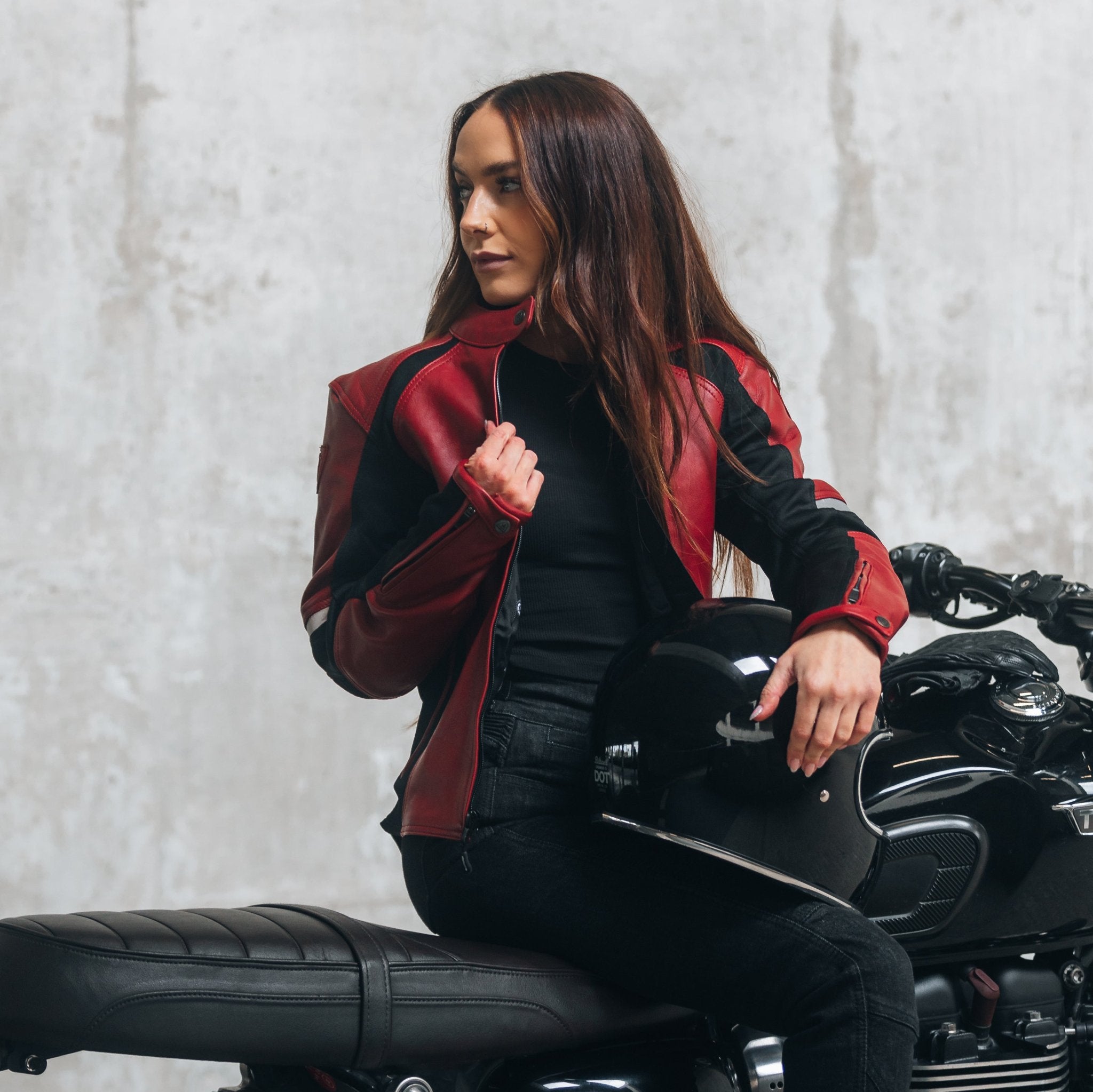 A young woman on her motorcycle wearing a red and black women's motorcycle jacket with reflectors on the sleeves.