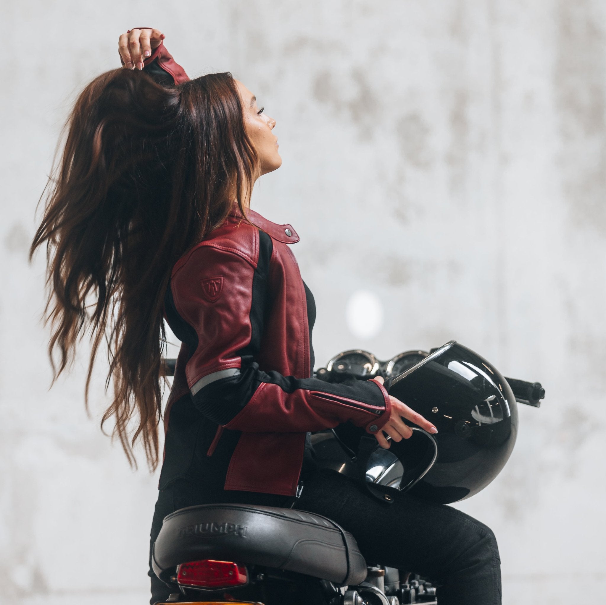 A young woman on her motorcycle wearing a red and black women's motorcycle jacket with reflectors on the sleeves.