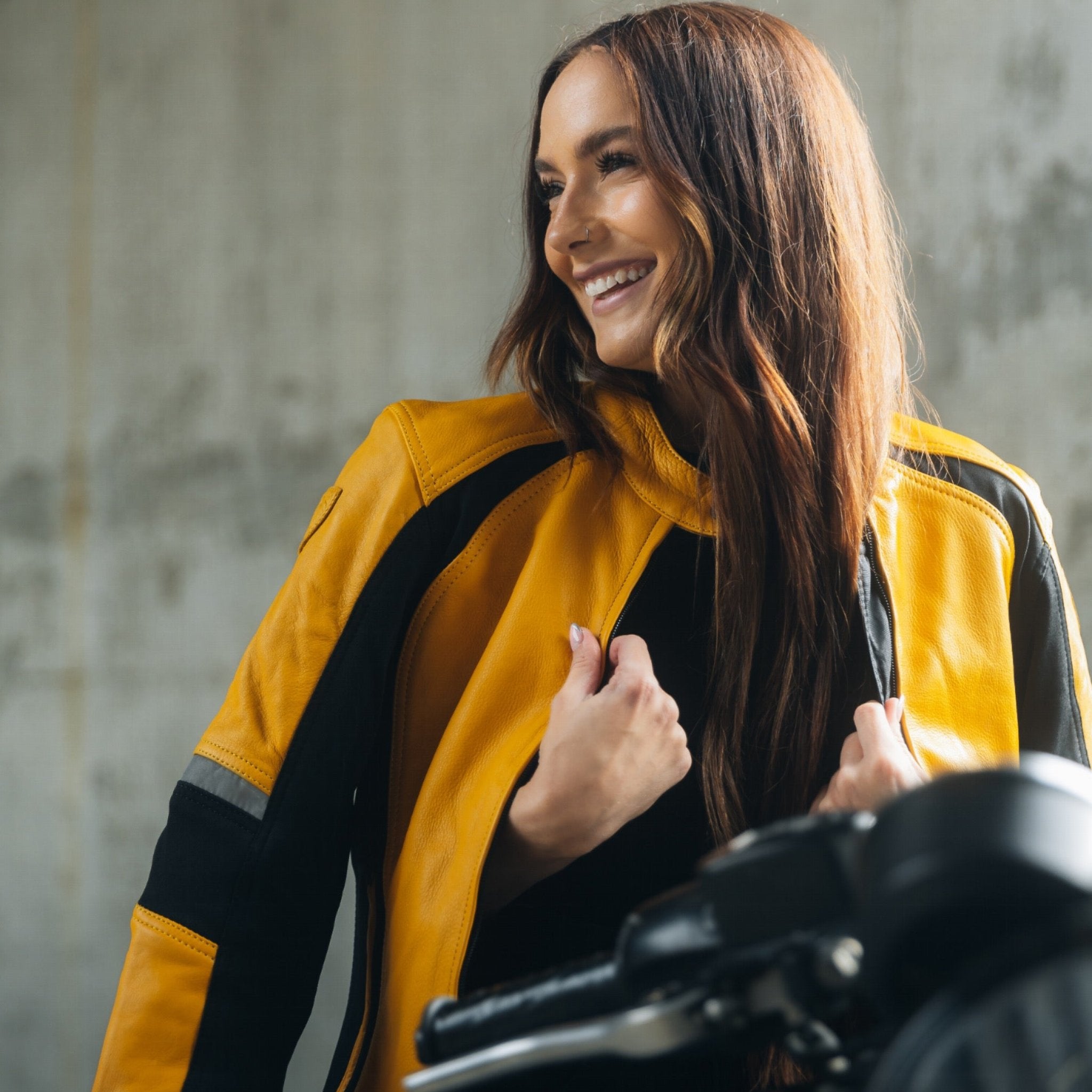 A young woman on her motorcycle wearing a red and black women's motorcycle jacket with reflectors on the sleeves.