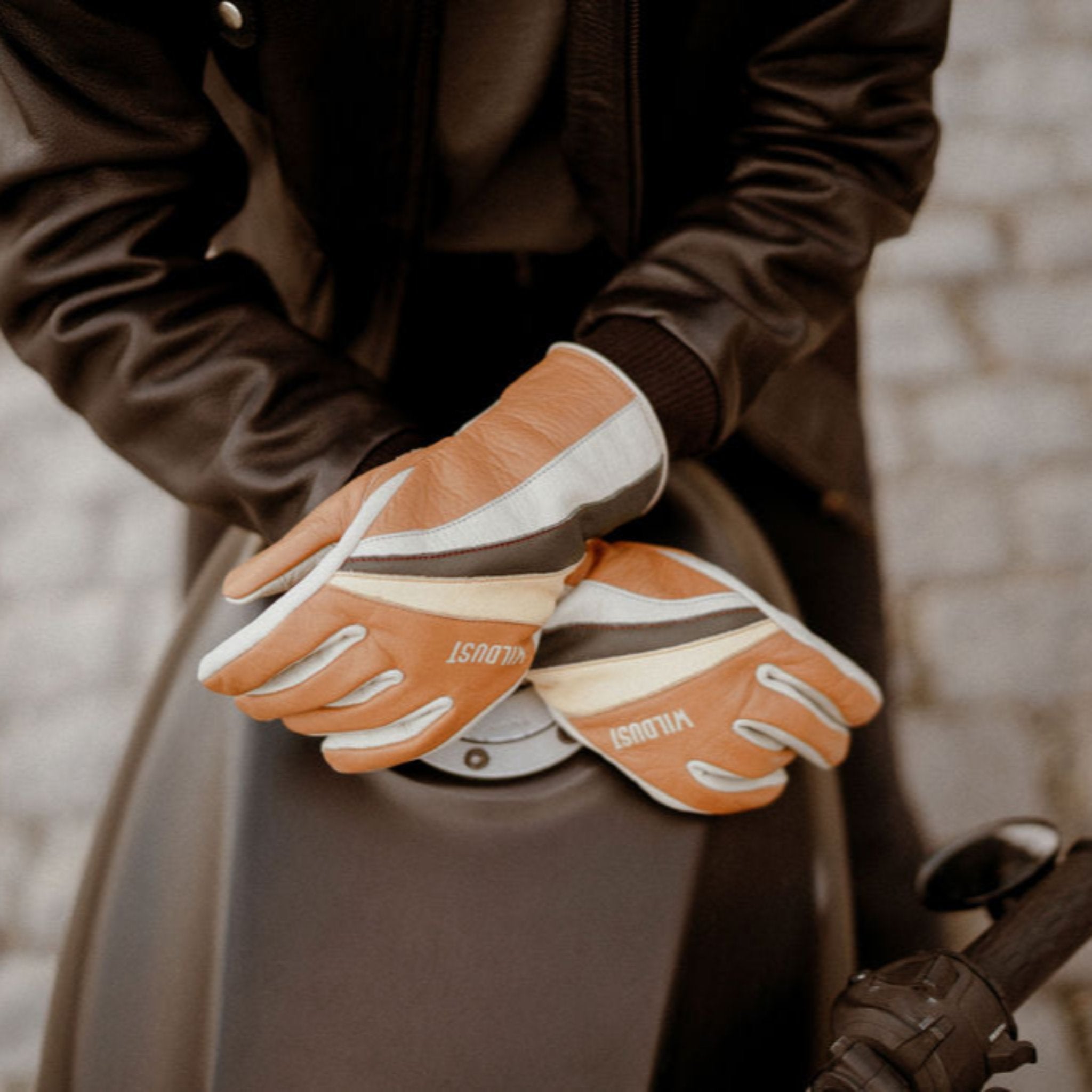 women&#39;s hands over a motorcycle gas tank wearing colourful leather gloves from WILDUST