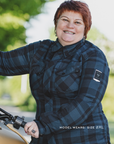 Person wearing a blue plaid shirt standing next to a motorcycle with a blurred green background