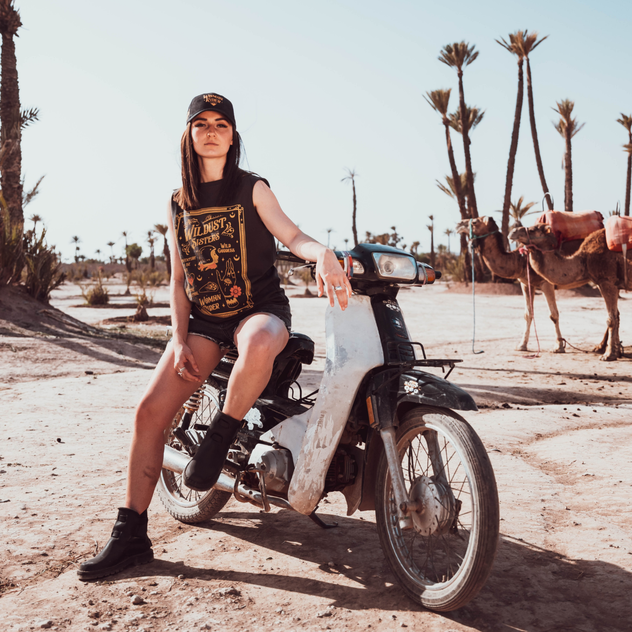 Woman sitting on a Motorcycle wearing a Black t-shirt with a woman wearing a Motorcycle helmet with the text &quot;Wildust sister&quot; 