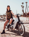 Woman sitting on a Motorcycle wearing a Black t-shirt with a woman wearing a Motorcycle helmet with the text "Wildust sister" 