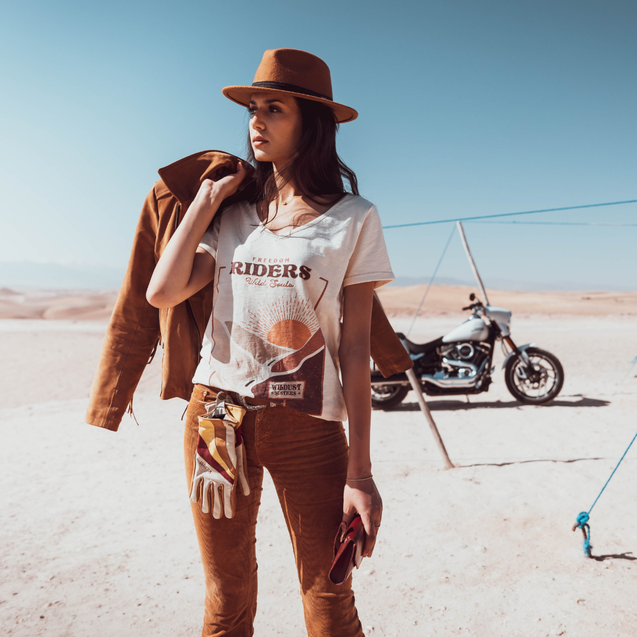 Woman standing in the dessert wearing a T-shirt with a sunset/sunrise print and the text &quot;Freedom Riders Wild Souls&quot; and &quot;Wildust sisters&quot;