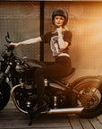 Woman sitting on a Motorcycle wearing  a T-shirt with a women wearing a Motorcyclehelmet print and with the text "Wild dust sisters woman rider" and "Speed Goddess"