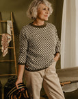 an older lady wearing a knitted khaki green and white jumper with chessboard motives  from Wildust