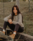 a young woman siting by the fence wearing a knitted khaki green and white jumper with chessboard motives  from Wildust