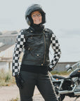 Smiling woman standing outside in front of a motorcycle, wearing motorcycle clothing and a black knitted neck warmer from Moto Girl.