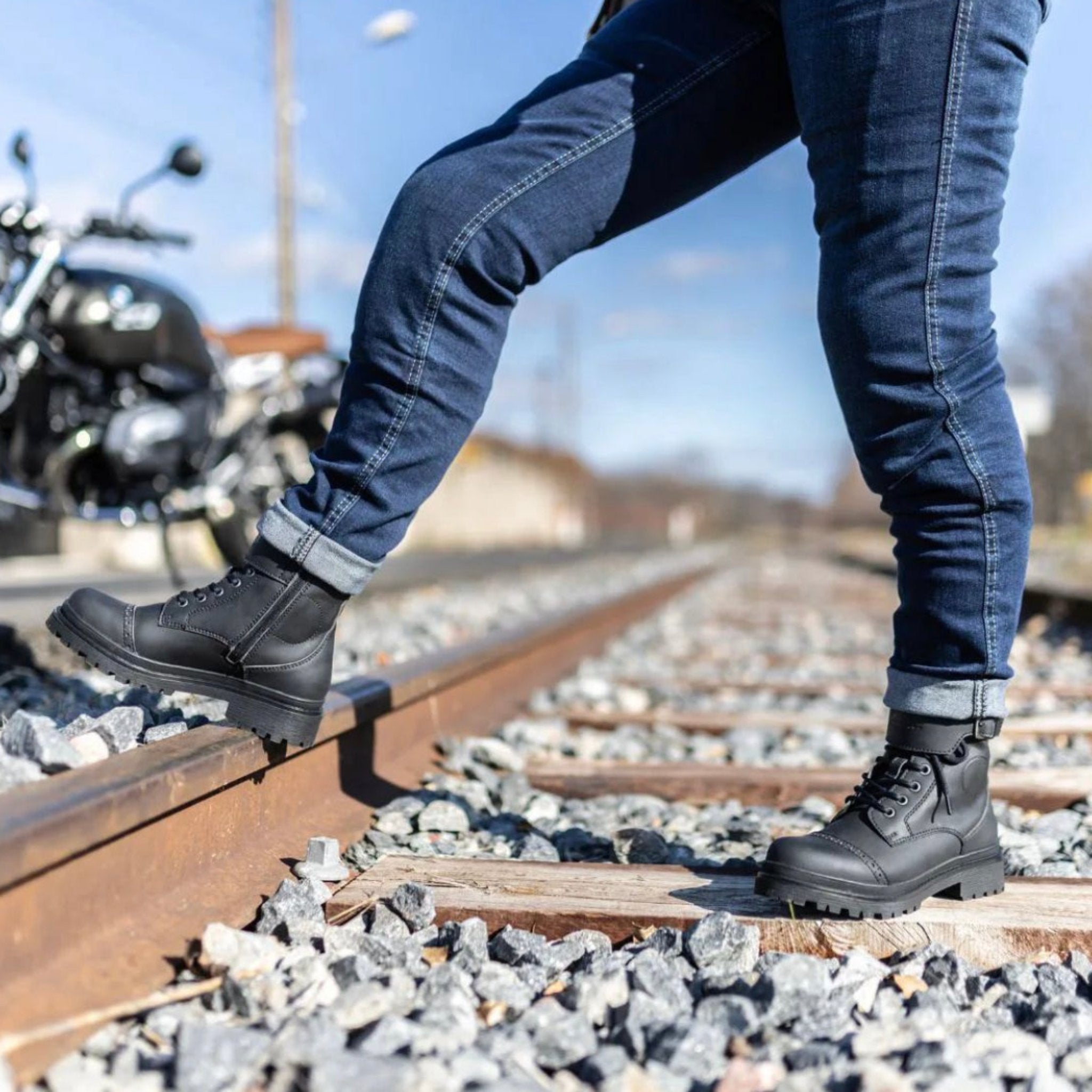 Woman&#39;s legs standing on the railway and wearing black motorcycle boots