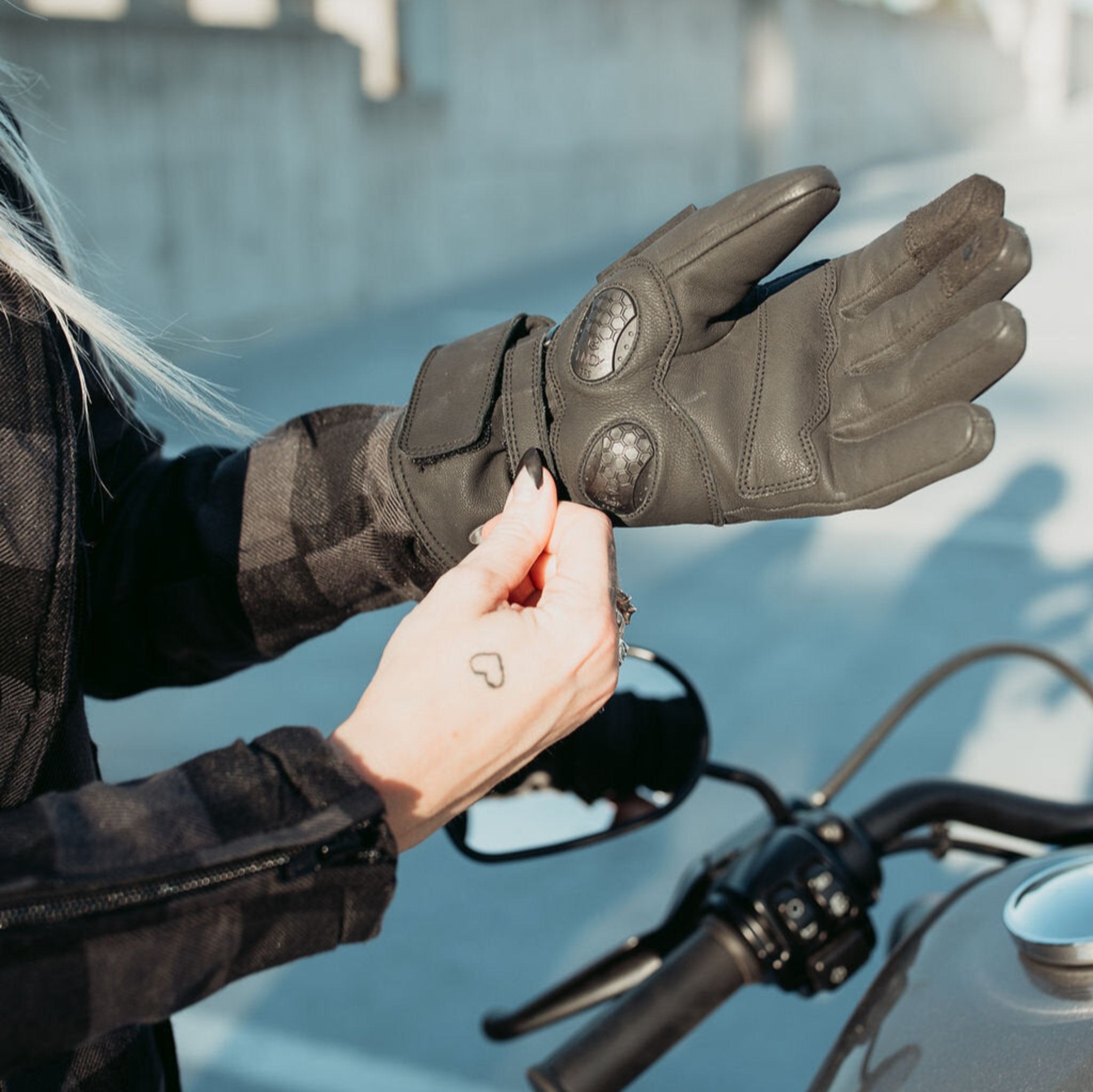 Woman standing outside wearing the Nandi gloves from Motogirl while adjusting the velcro closure on the wrist.