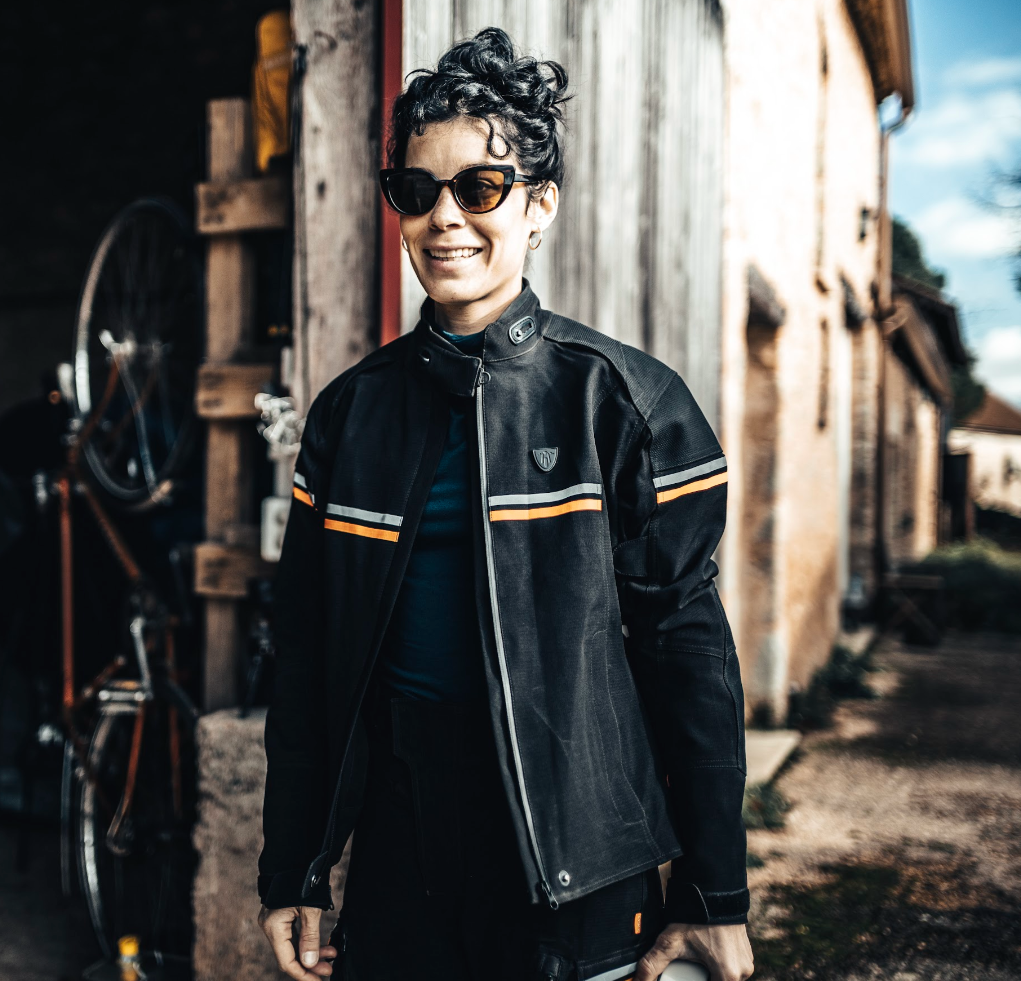 a woman with sunglasses wearing black textile mc jacket with orange and grey details