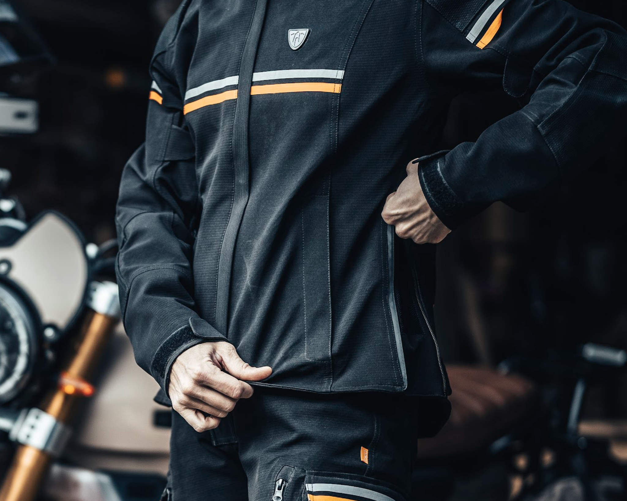 woman's hand zipping side zipper on her black textile mc jacket with orange and grey details