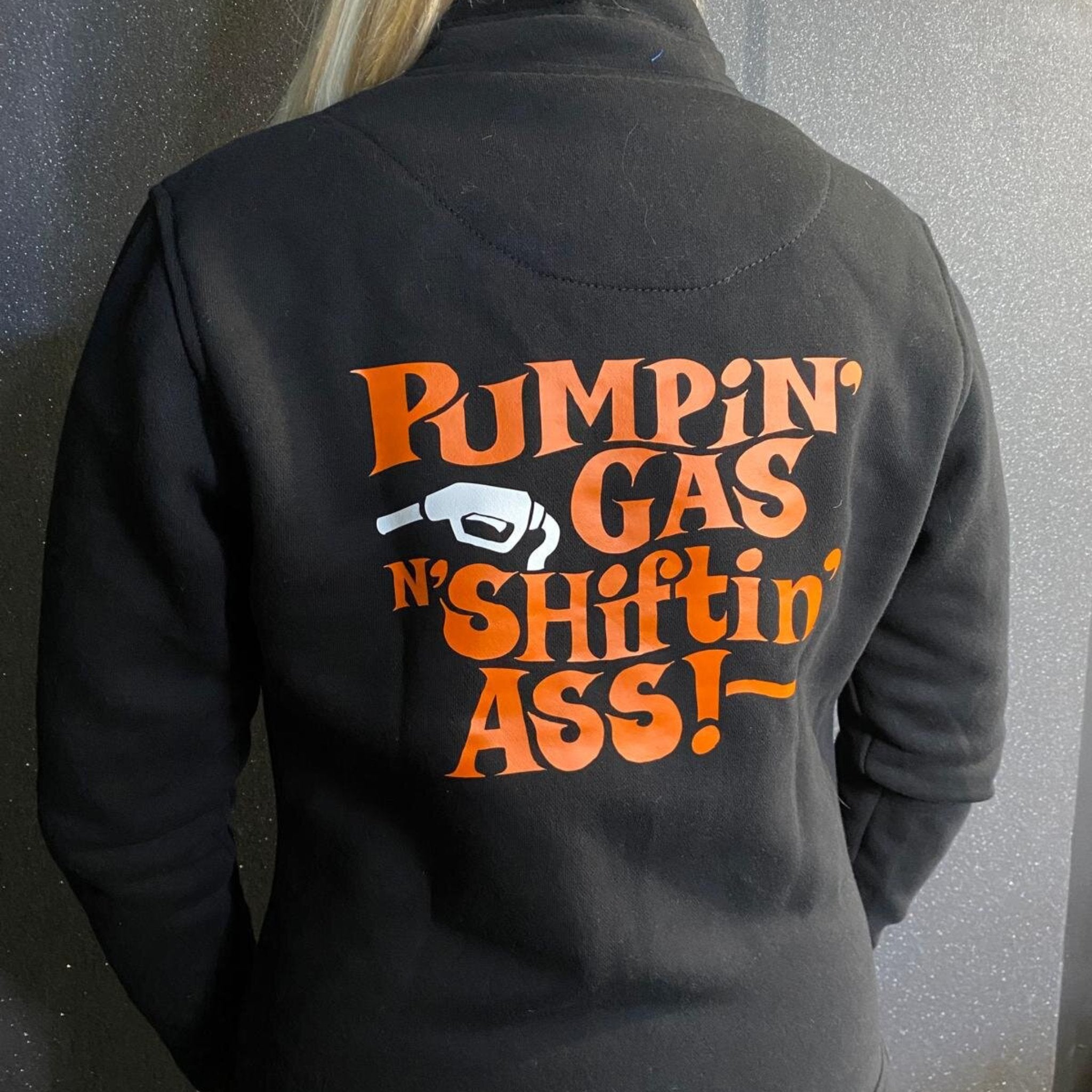 A woman wearing black lady sweatshirt with orange &quot;pumping gas shifting ass&quot;motive on the back