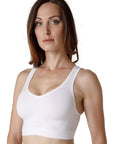 A dark-haired woman wearing a white sports bra with wide straps from Tremonte. 