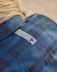 Close-up of a person wearing a blue plaid shirt with a brand logo  SHIMA on the chest.