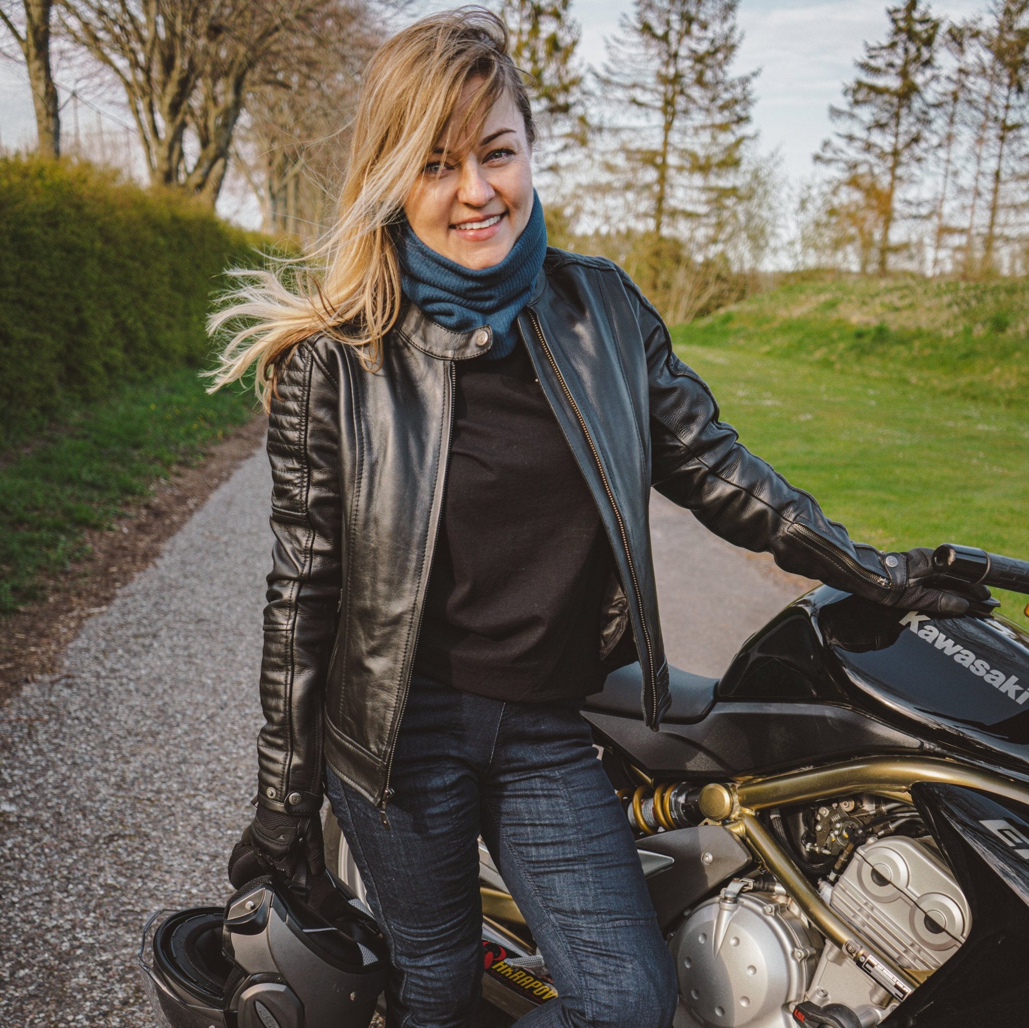 A young woman standing by her Kawasaki motorcycle wearing black leather jacket