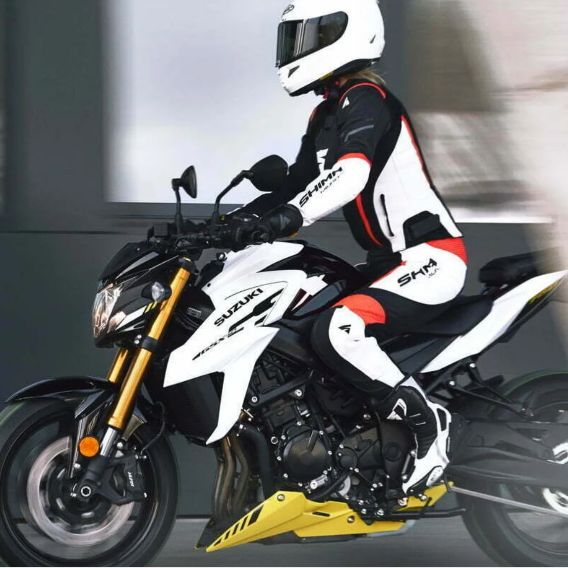 A woman on a white Suzuki motorcycle wearing SHIMA MOTORCYCLE LEATHER suit IN BLACK FLUO, WHITE AND RED FLUO