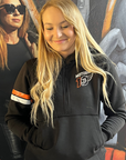 Person wearing a black hoodie with a logo, standing in front of a colorful mural.
