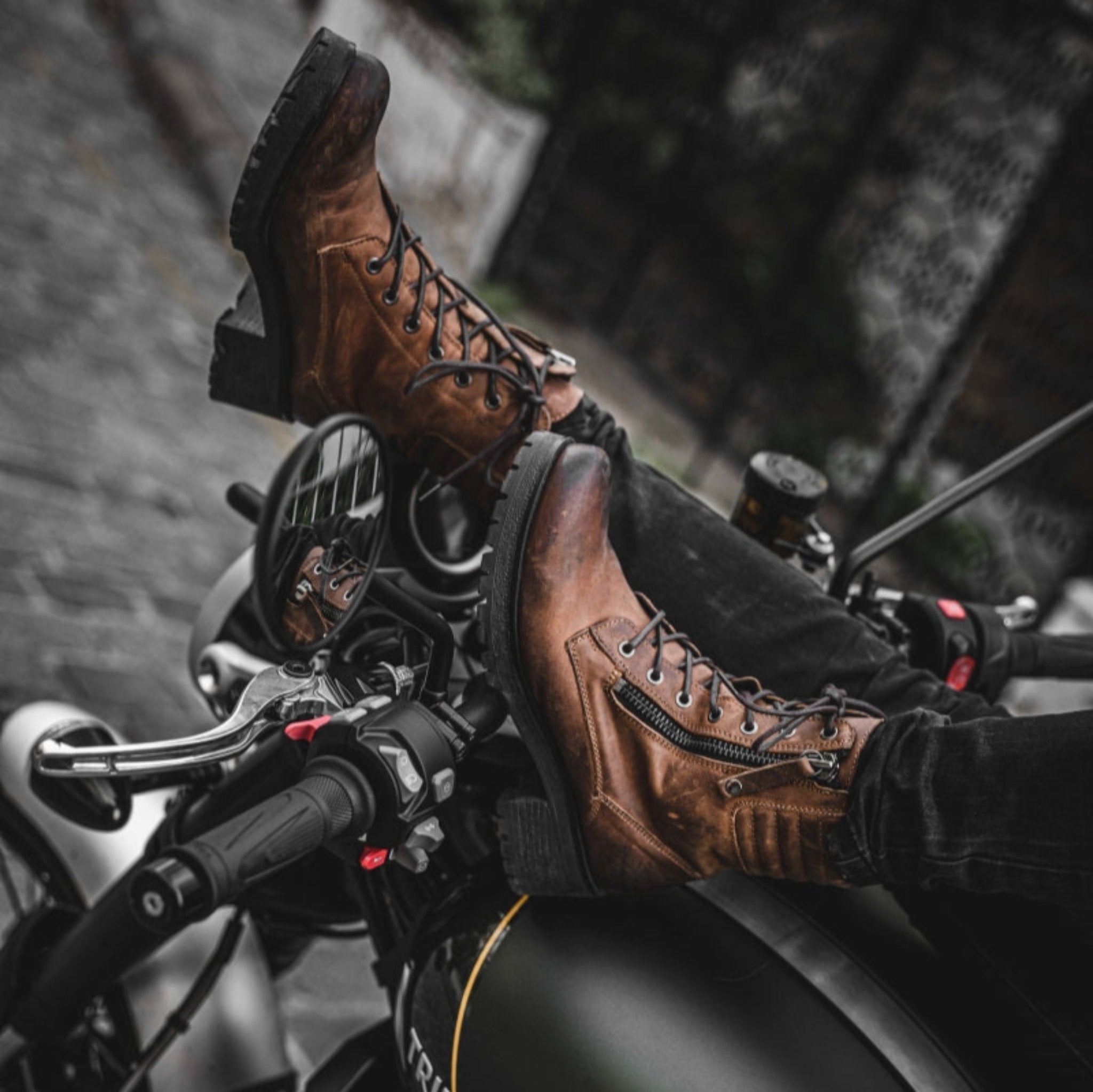 women&#39;s feet resting on motorcycle steering wheel, wearing brown leather mc boots 