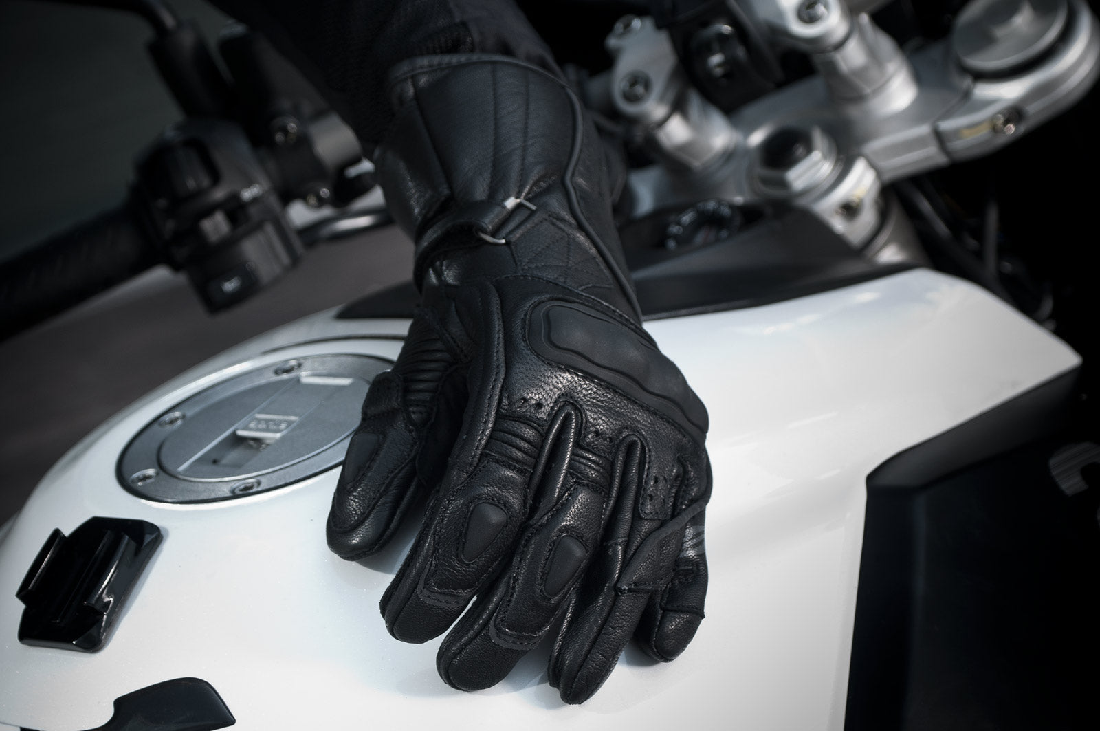 A  woman's hand with black waterproof motorcycle glove on a white motorcycle  tank 