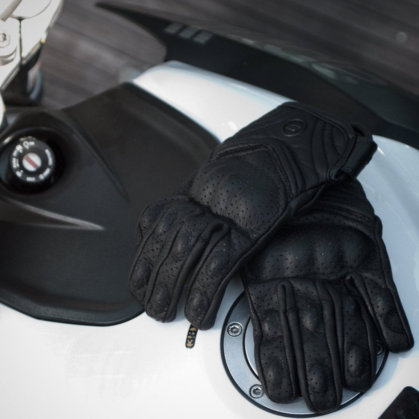 Black leather women&#39;s motorcycle gloves from Shima on a tank of a white motorcycle 