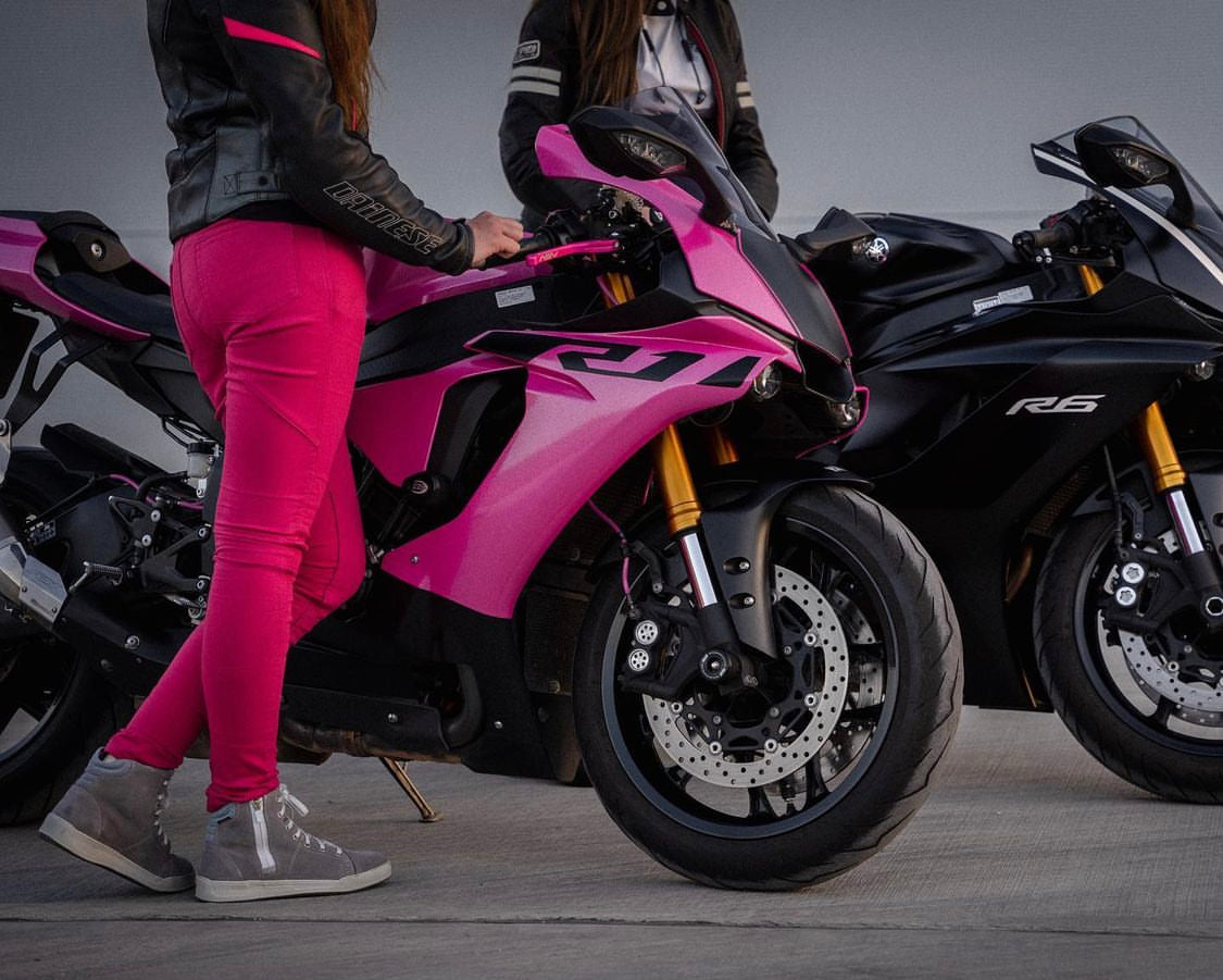 A woman wearing pink motorcycle trousers standing by a pink motorcycle