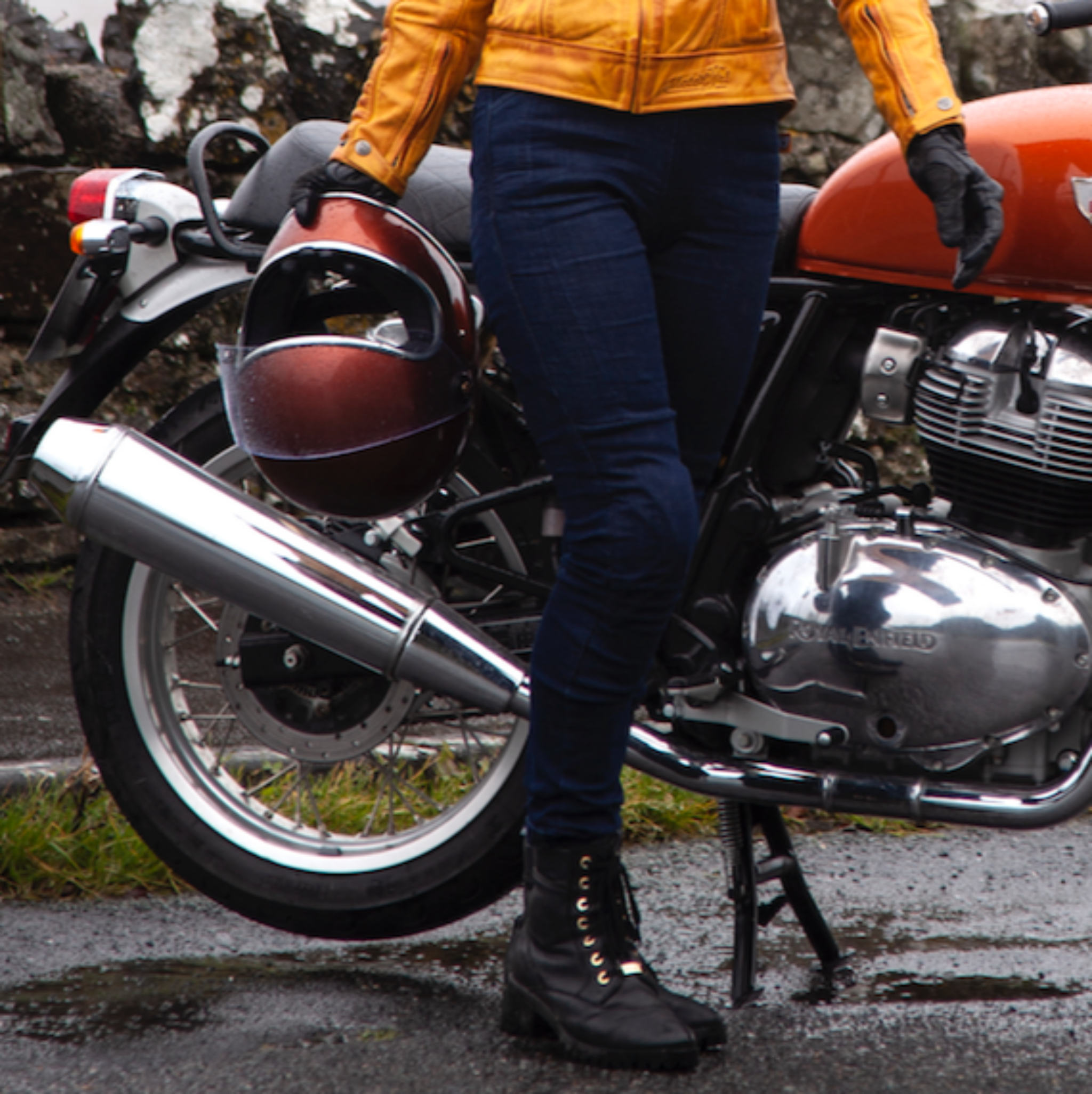 A woman wearing blue motorcycle jeans and carrying a helmet