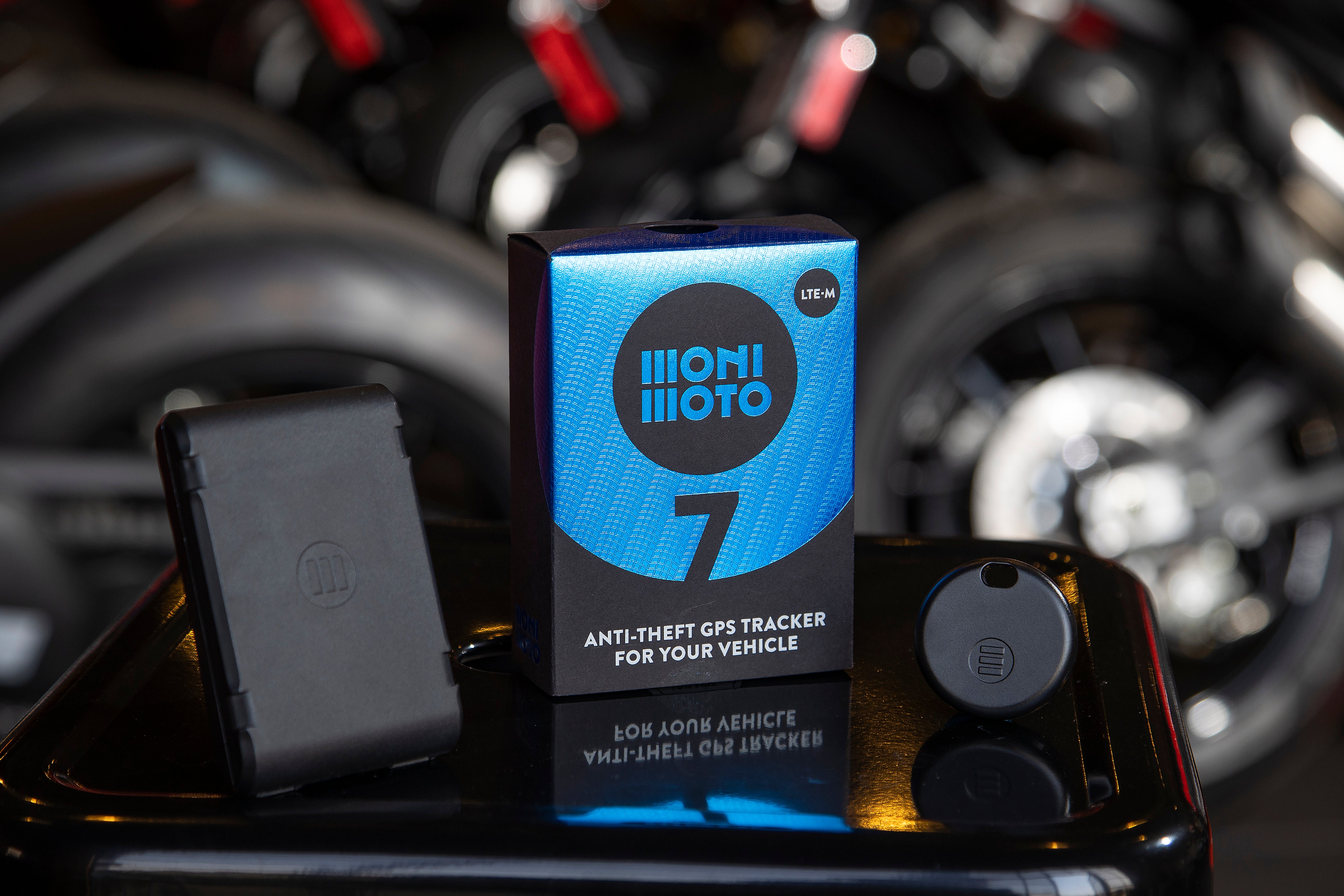 MoniMoto Motorcycle black and small GPS tracker places on the table with a motorcycle in a background