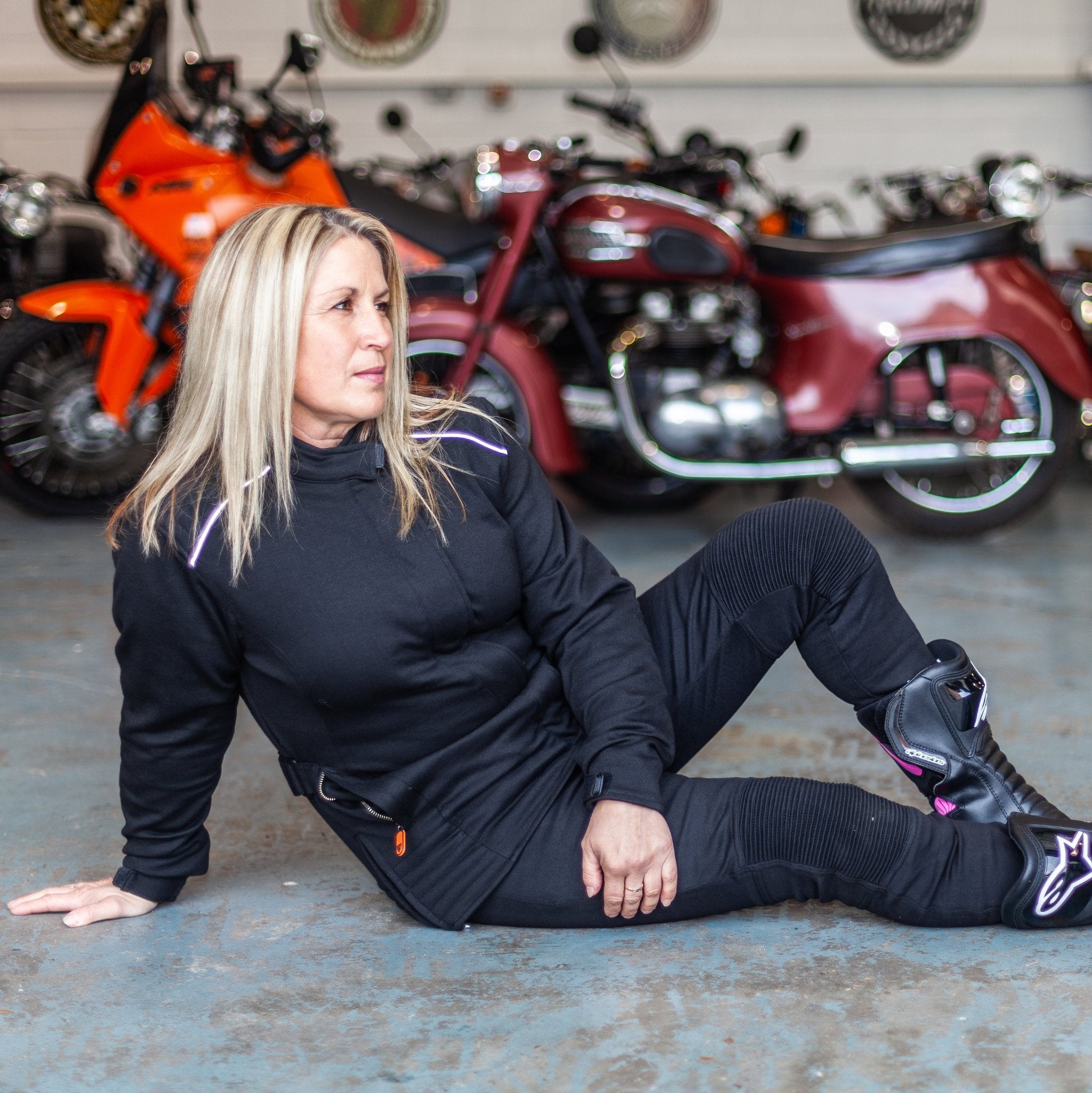 A blong woman sitting on the floor by motorcycles wearing women&#39;s motorcycle jacket from Moto Girl 