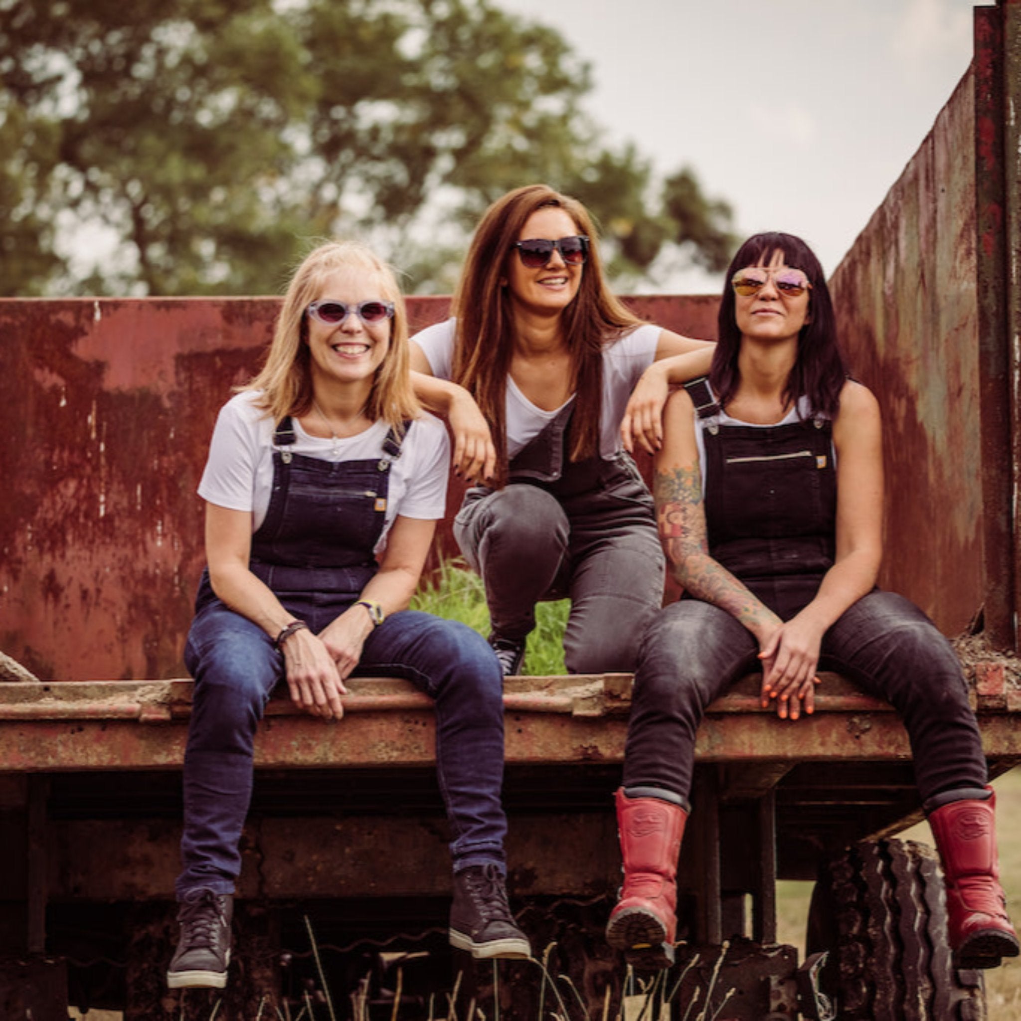 Three women wearing motorcycle overalls siting on the back of a truck