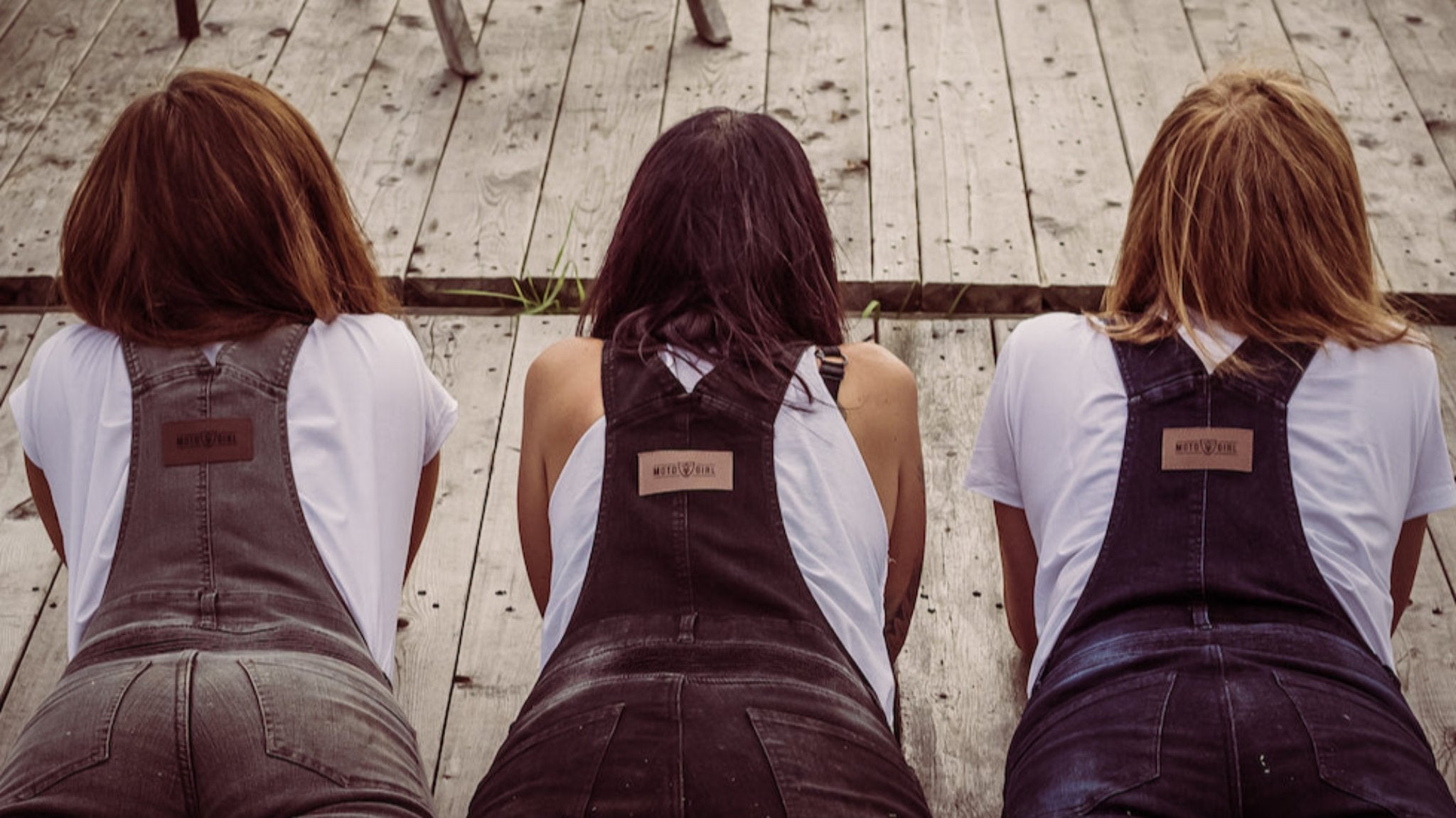 Three women wearing motorcycle overalls laying on the wooden floor