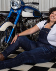 A smiling woman siting on the floor in the motorcycle shop and wearing blue motorcycle overall 
