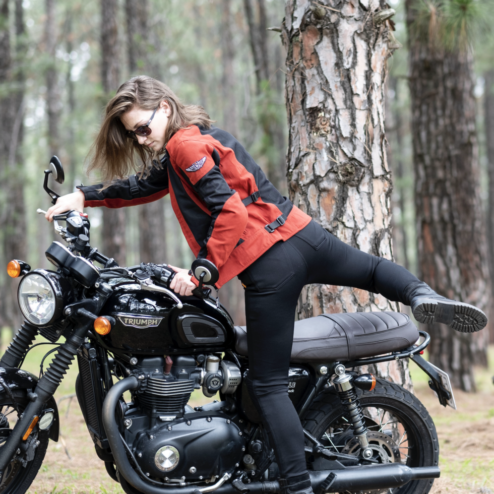 a young woman getting on a Triumph motorcycle wearing red and black women&#39;s motorcycle summer jacket from Moto Girl 