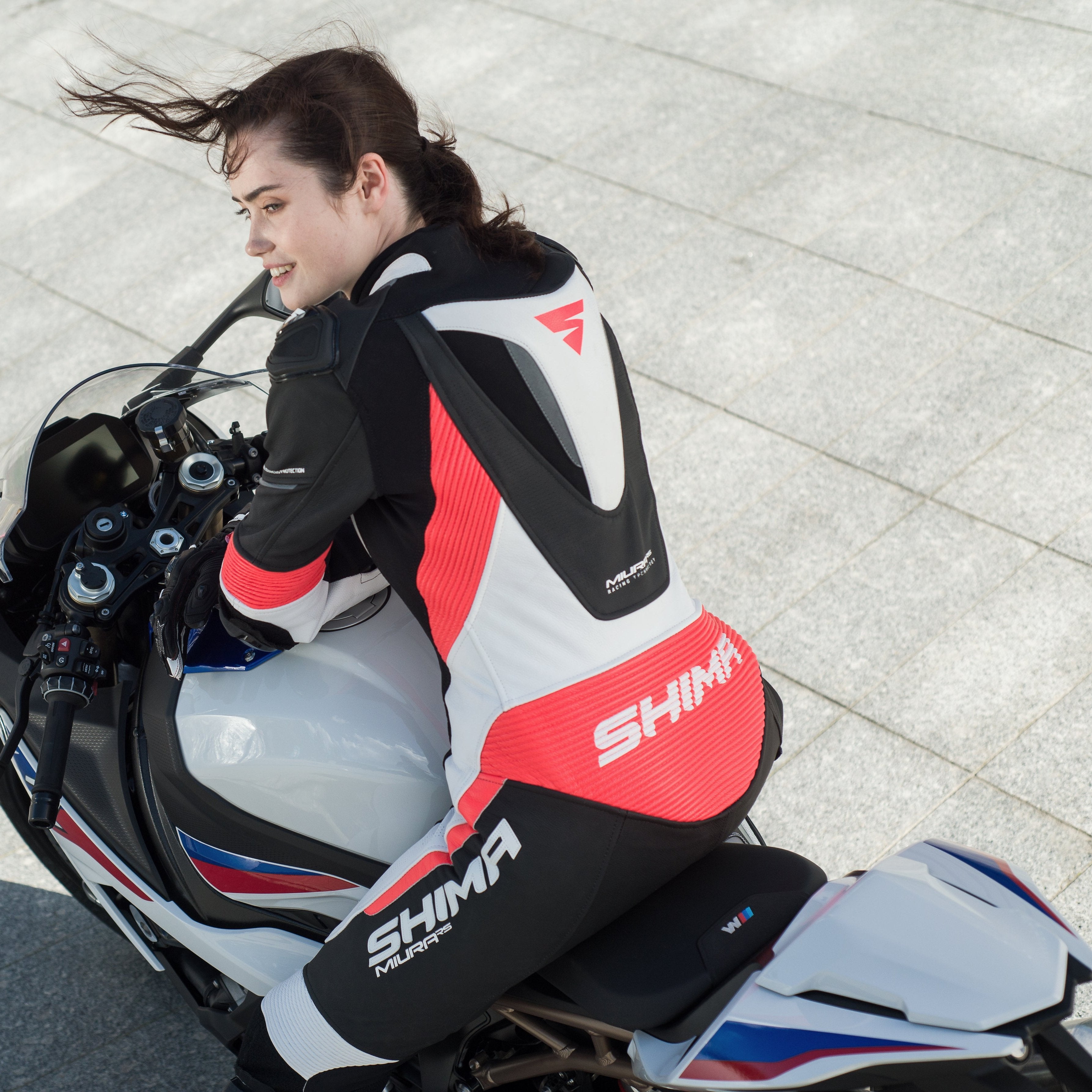 A woman on a motorcycle wearing Women&#39;s racing suit MIURA RS in black, white and fluo from Shima 