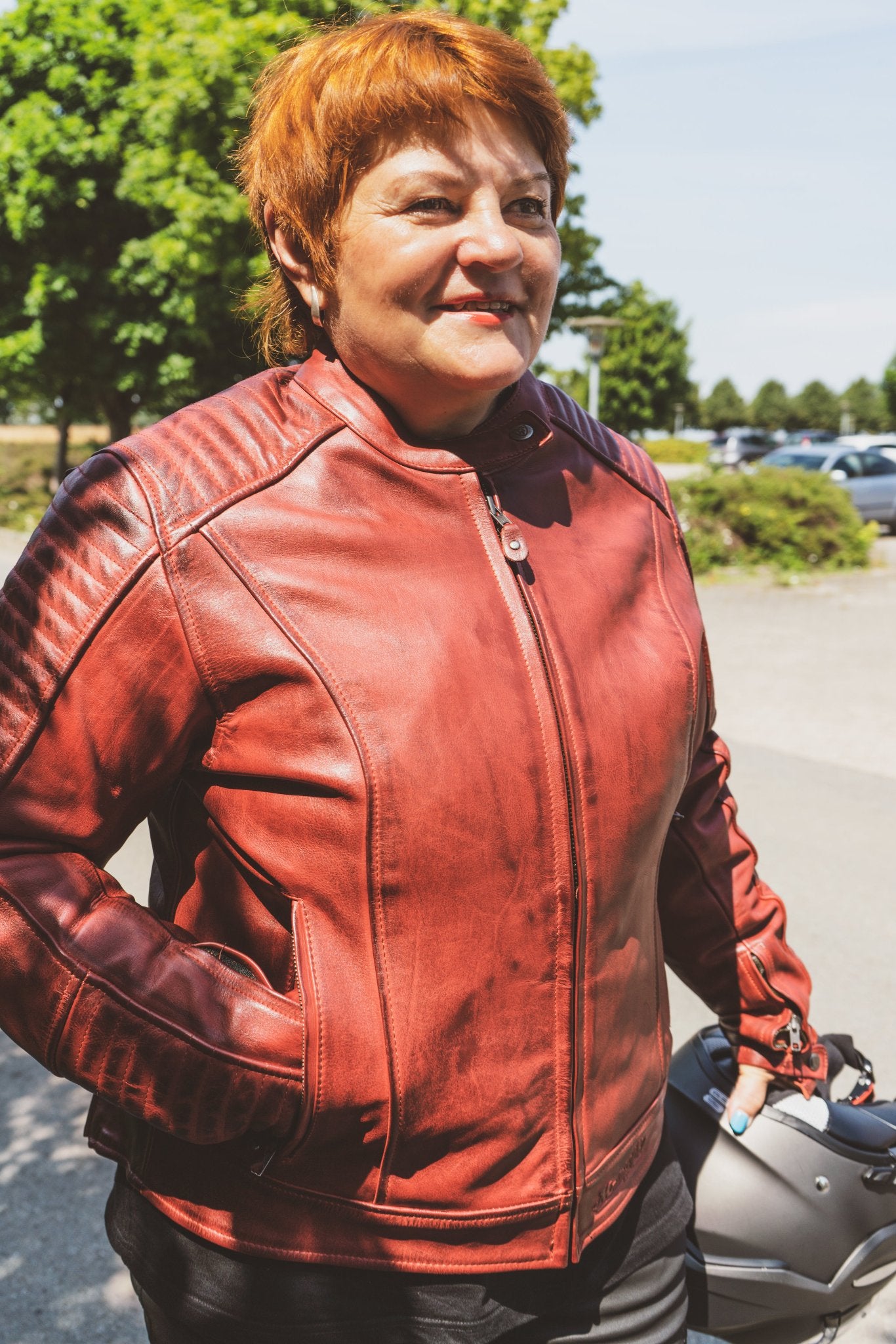 smiling red haired woman holding a helmet and wearing a red Valerie motorcycle jacket 