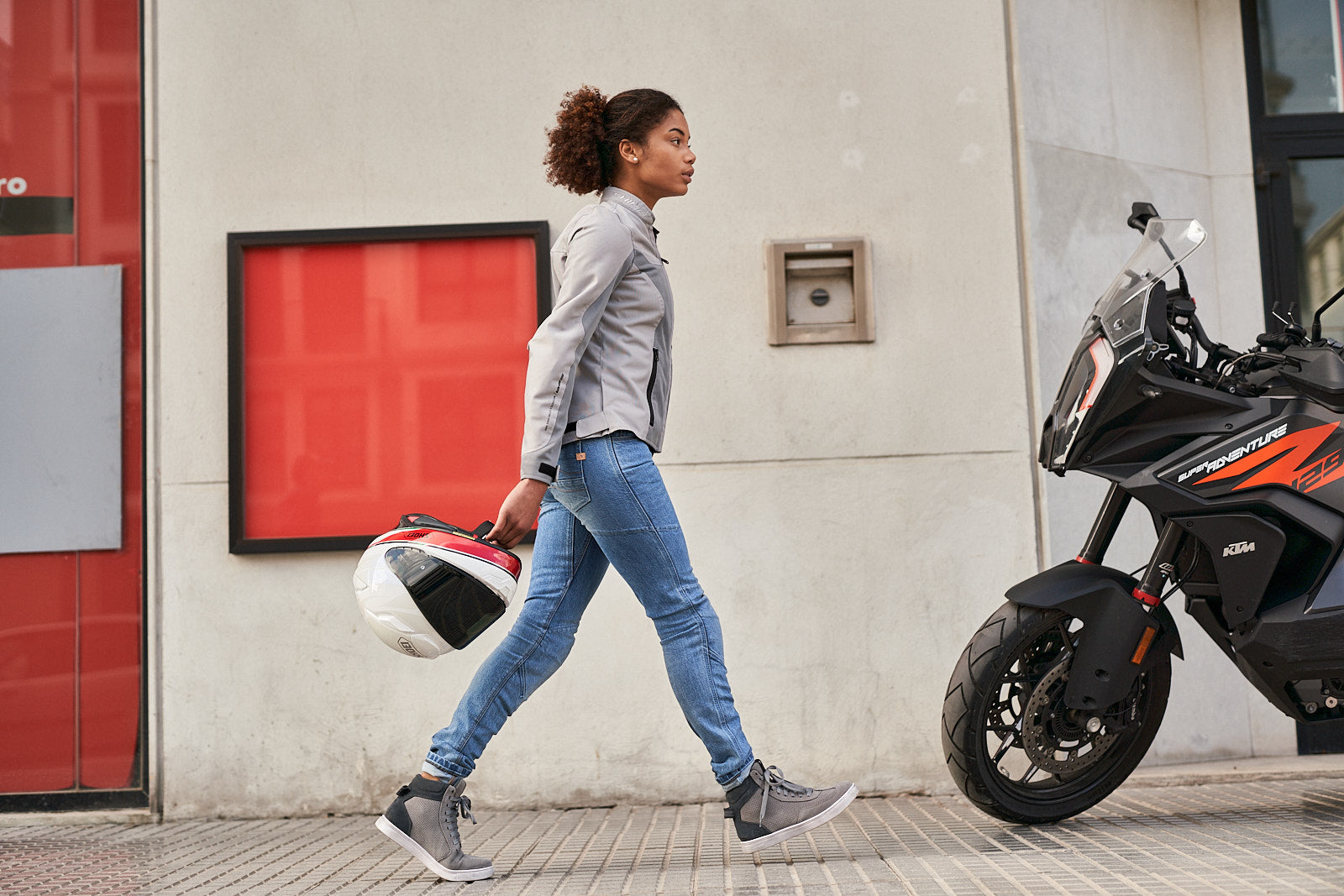 Young woman wearing Light blue motorcycle jeans for women walking towards her motorcycle