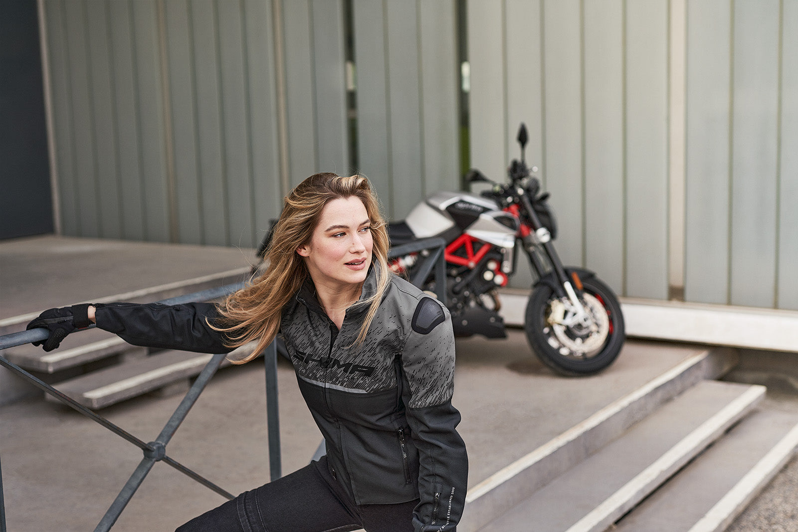 A blond woman near the motorcycle wearing grey women&#39;s motorcycle jacket from SHIMA