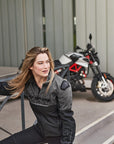 A blond woman near the motorcycle wearing grey women's motorcycle jacket from SHIMA