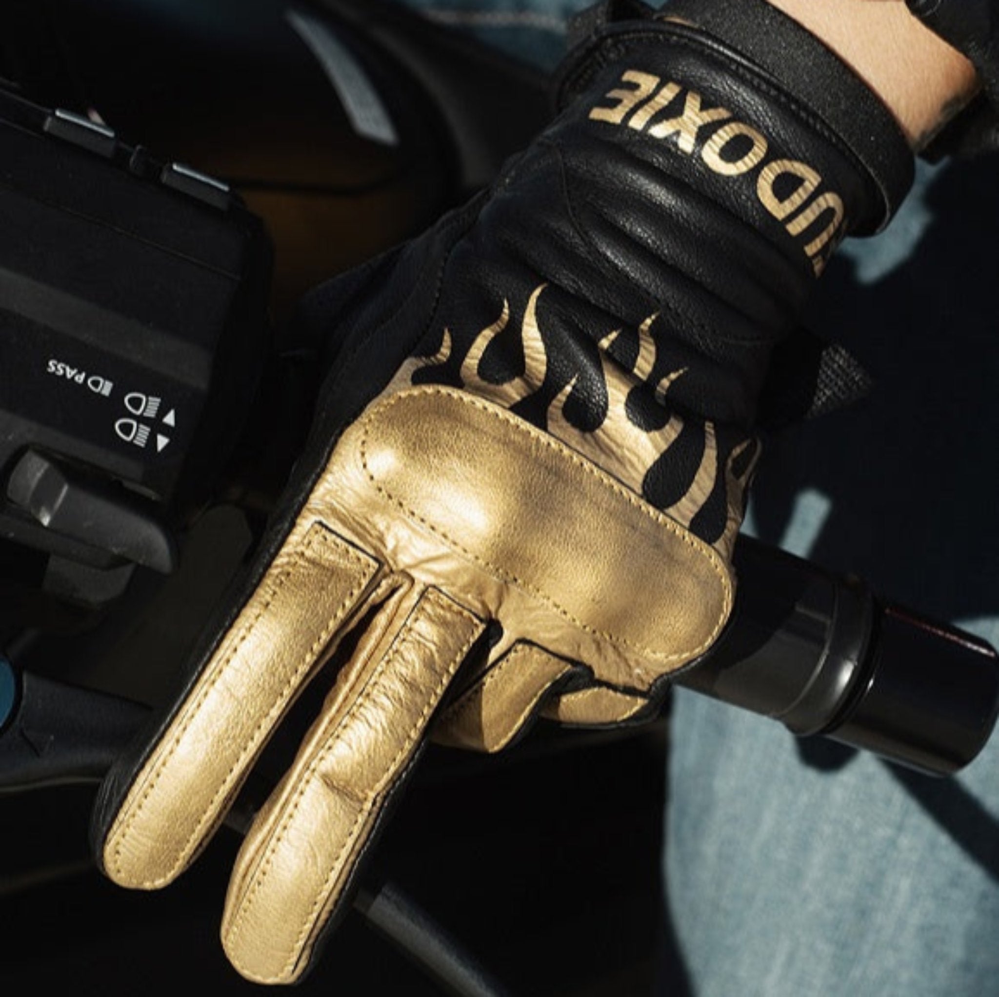 Woman&#39;s hand on a throttle wearing black Eudoxie mc glove with golden flames 