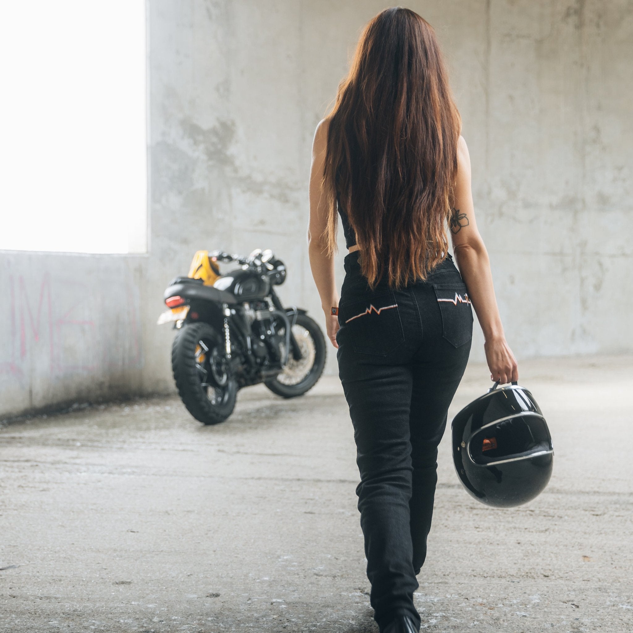 A woman walks towards her motorcycle wearing black women&#39;s motorcycle jeans from Moto Girl